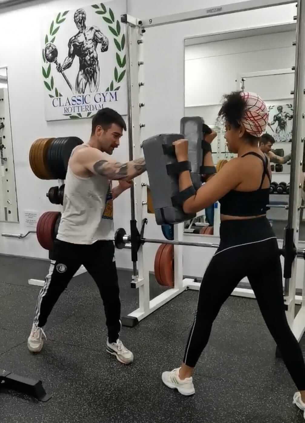 Een man en een vrouw trainen samen met bokspads, waarbij de man stoten uitvoert en de vrouw de pads vasthoudt voor een gestructureerde boks oefening.