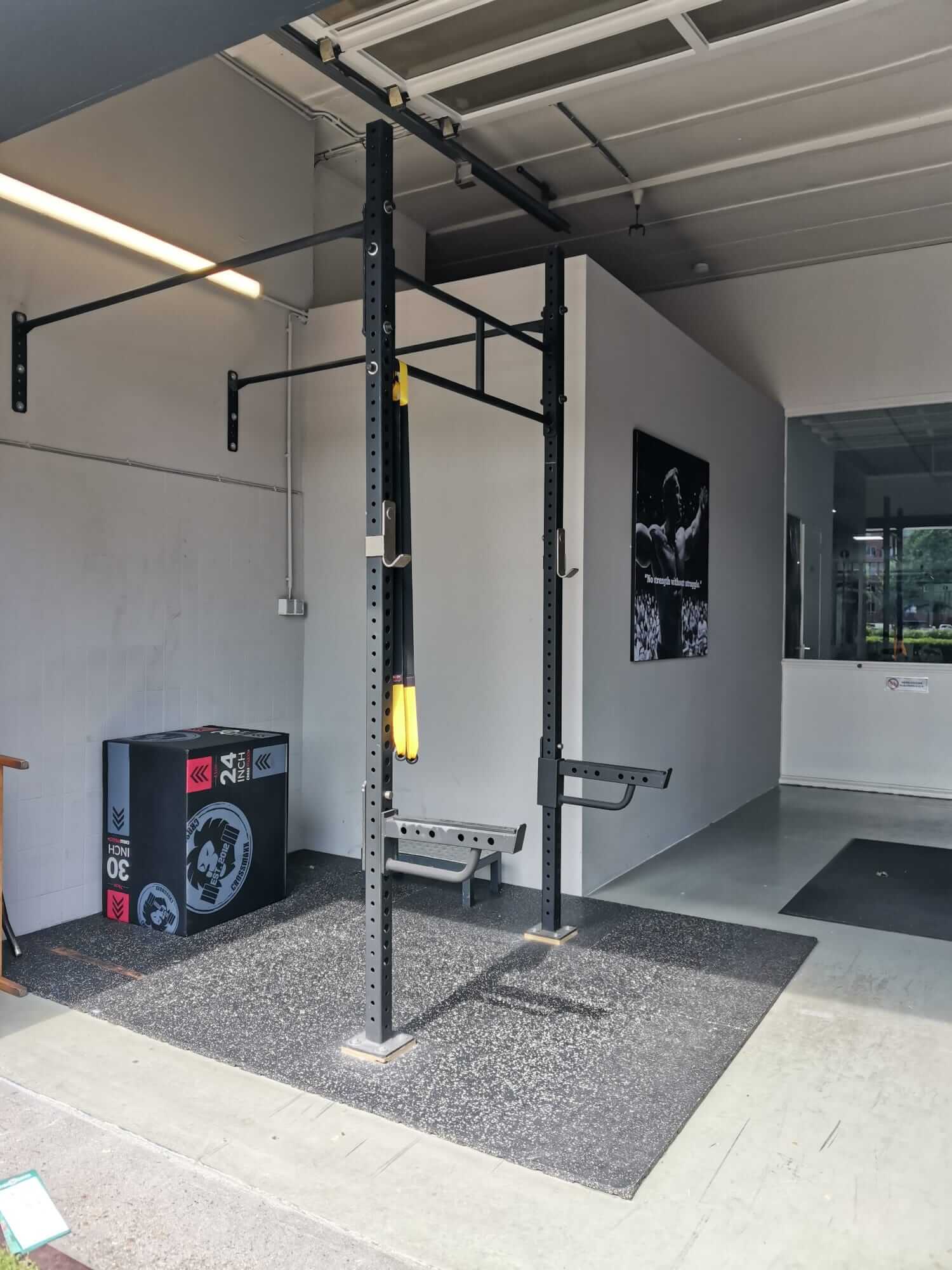 Binnenkomst in de gym start met een robuust crossfit rack, klaar voor krachttraining en functionele oefeningen."