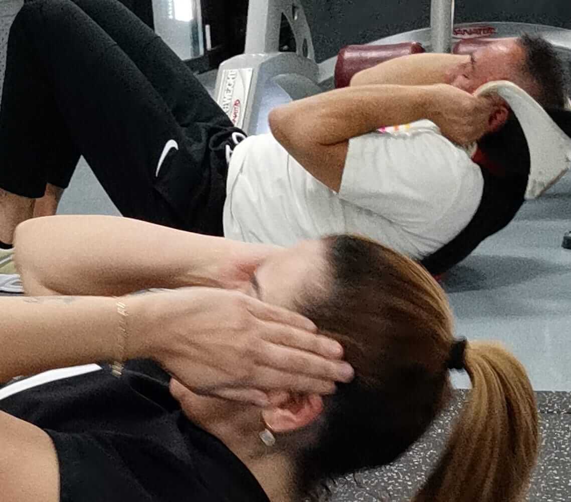 Een man en een vrouw voeren synchroon crunches uit tijdens een buikspiertraining in de sportschool, gefocust op hun core-strength