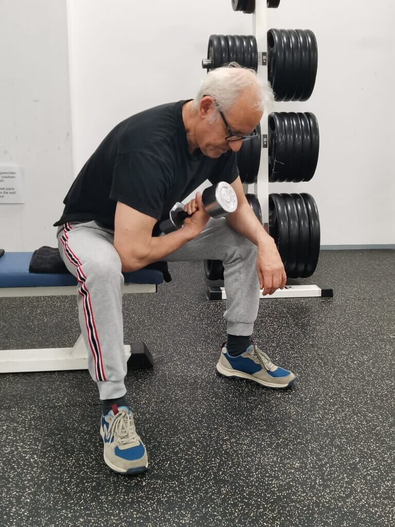 Senior voert een Concentration Dumbbell Curl uit – Een 65 vitaal+er traint de biceps met een gecontroleerde dumbbell curl.