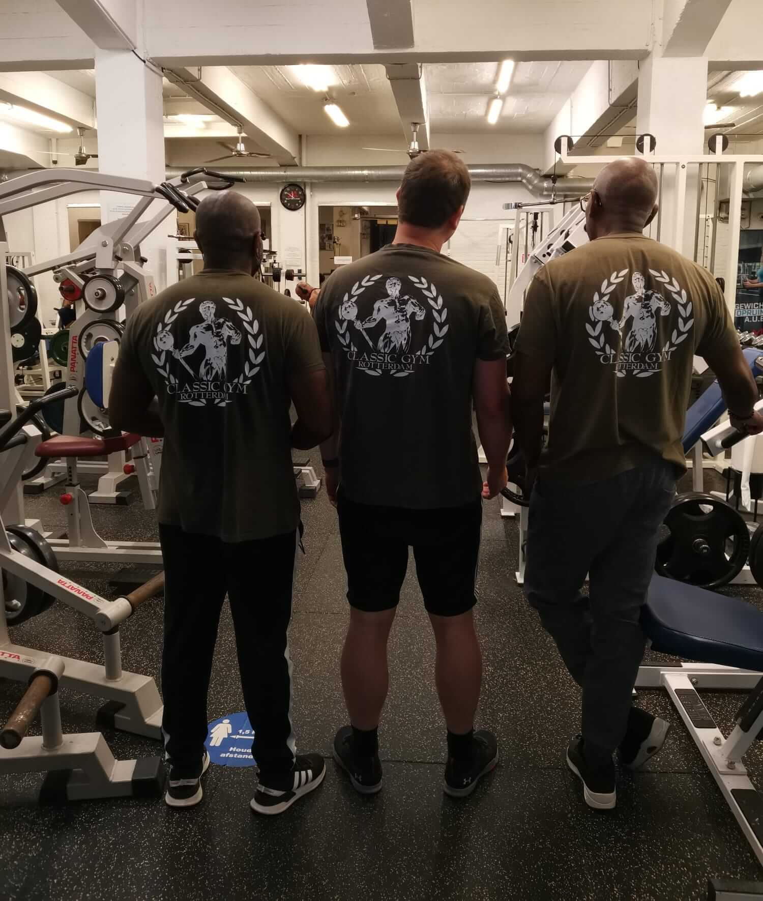 Drie sportieve familie leden naast elkaar in Classic Gym-shirts met het logo trots zichtbaar op de rug.