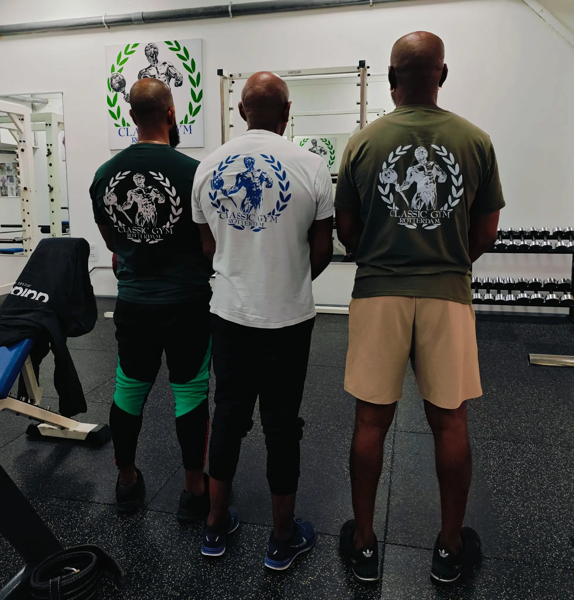 Drie sportende familie leden naast elkaar in Classic Gym-shirts met het logo trots zichtbaar op de rug.