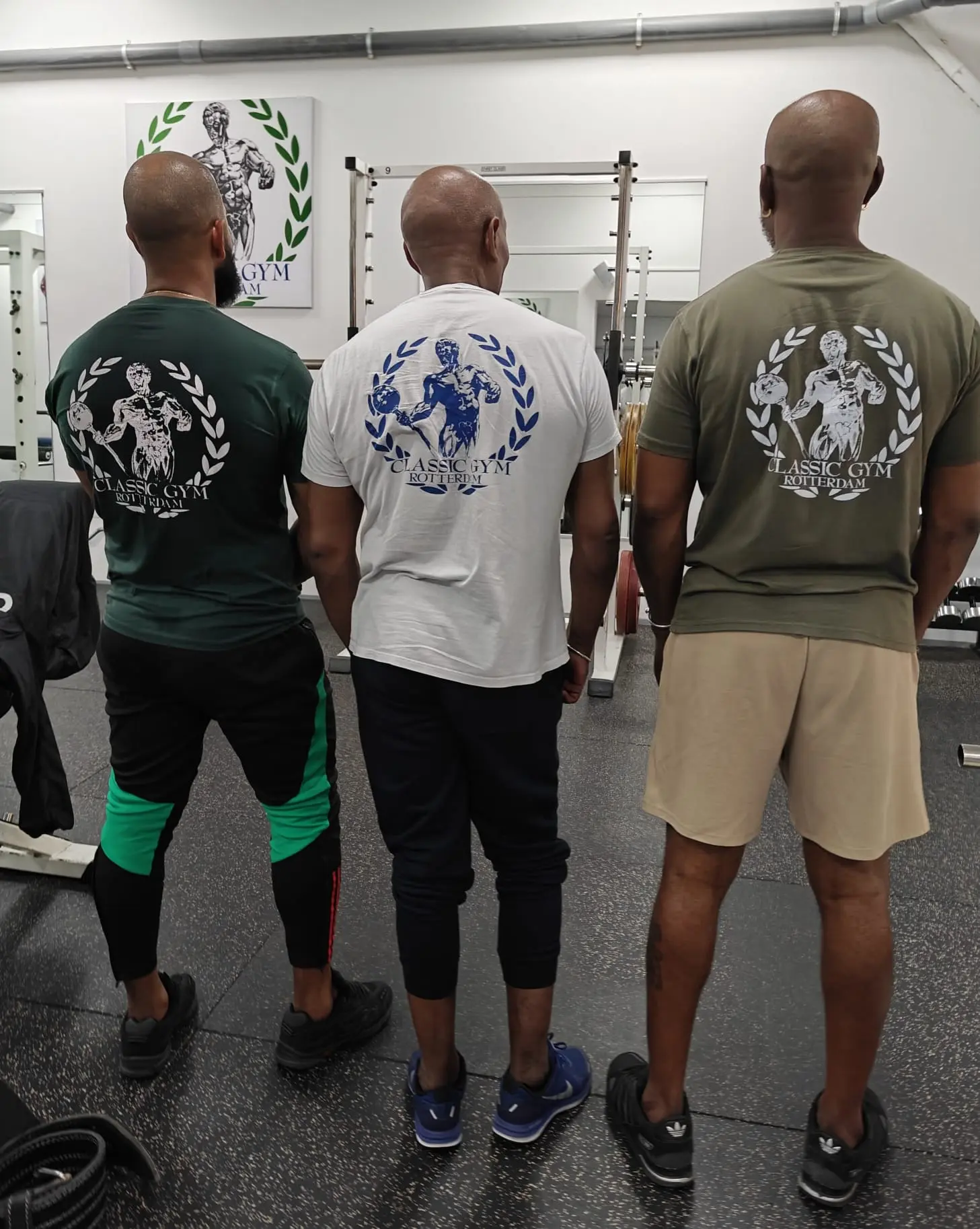 Drie sportende familie leden naast elkaar in Classic Gym-shirts met het logo trots zichtbaar op de rug.